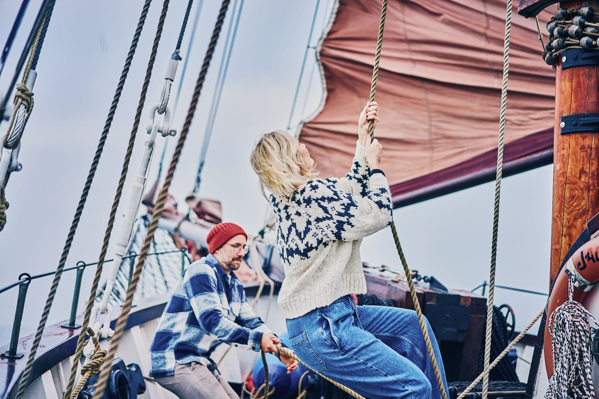 Menschen an Bord eines Segelschiffs, die gemeinsam die Segel setzen.