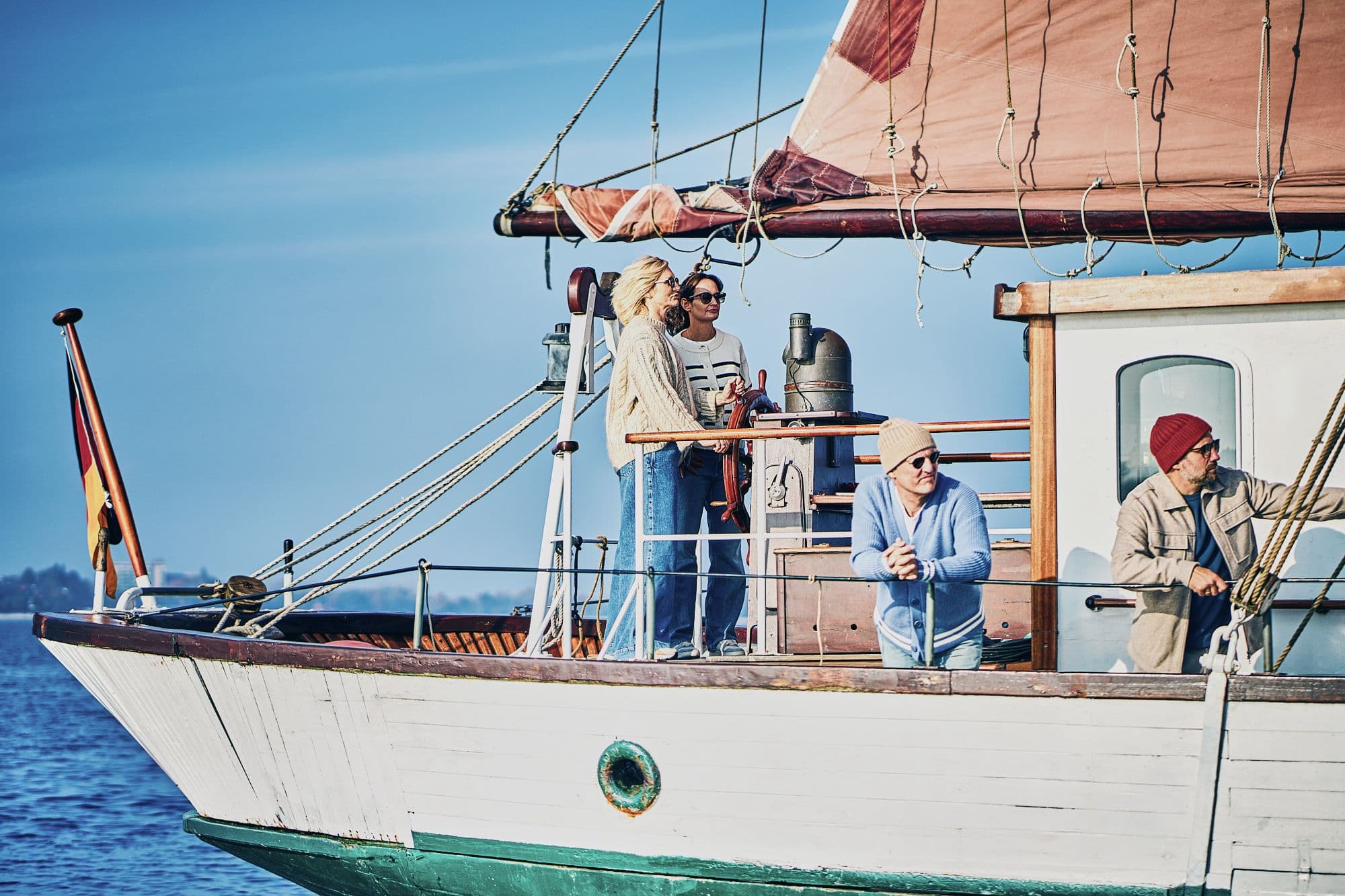 Menschen an Bord eines Segelschiffs, eine Person am Steuer, während die anderen die Aussicht genießen und das Schiff steuern.
