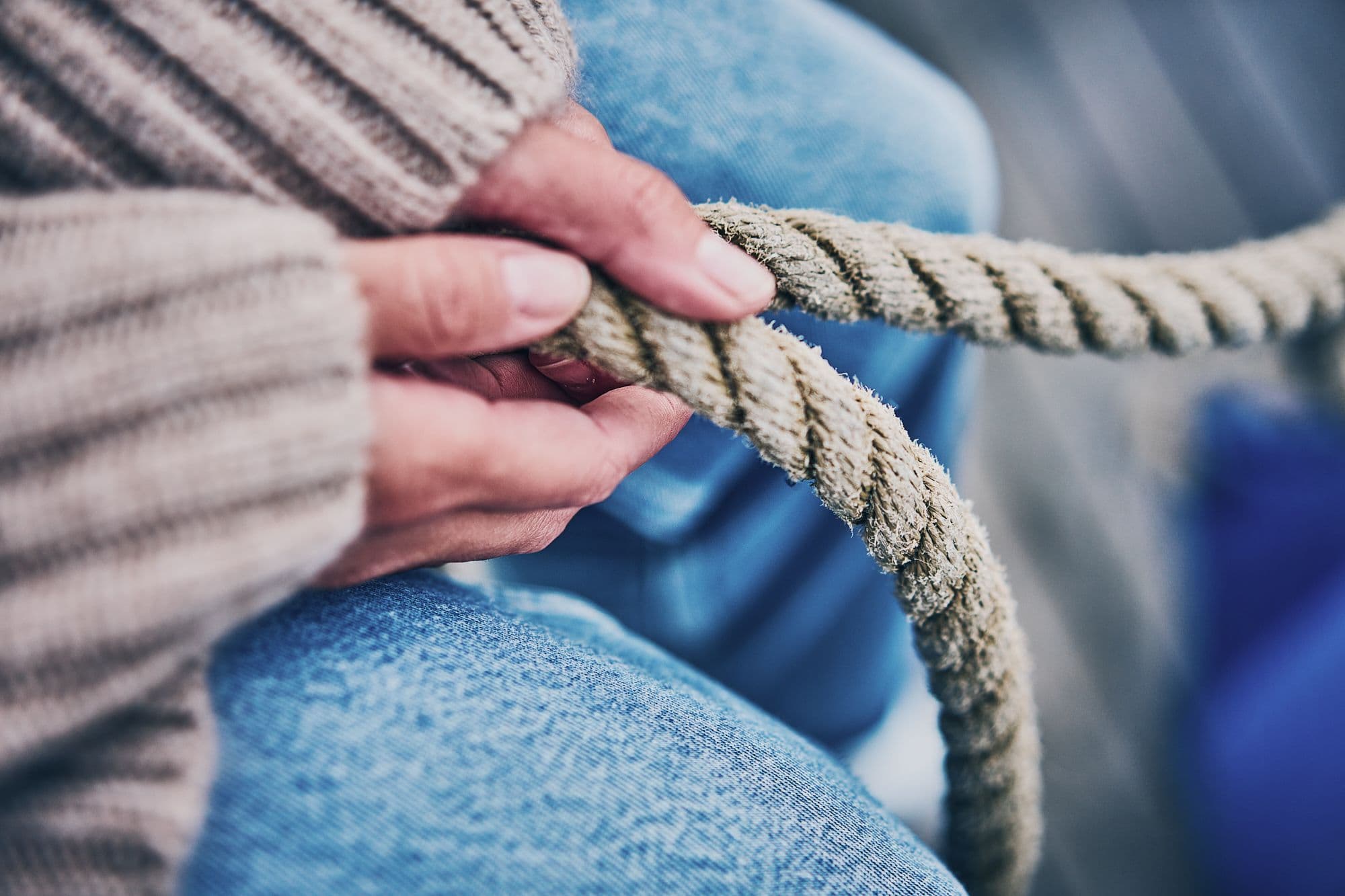 Nahaufnahme von Händen, die ein dickes, raues Seil festhalten, mit einem Wollpullover und Jeans im Hintergrund.